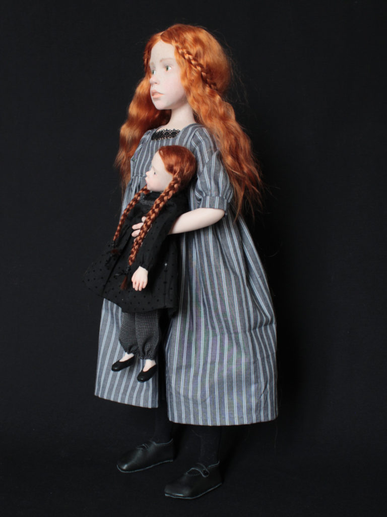 "Petite fille rousse portant une poupée habillée en noir"
